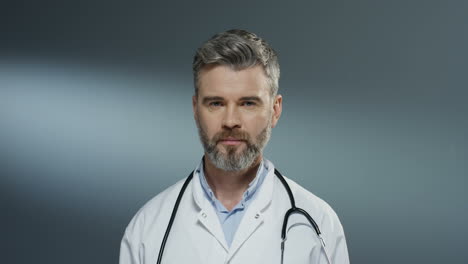 Close-up-of-the-Caucasian-good-looking-happy-and-smiled-man-doctor-in-white-gown-and-with-stethoscope-on-his-neck-looking-straight-to-the-camera.-Portrait.